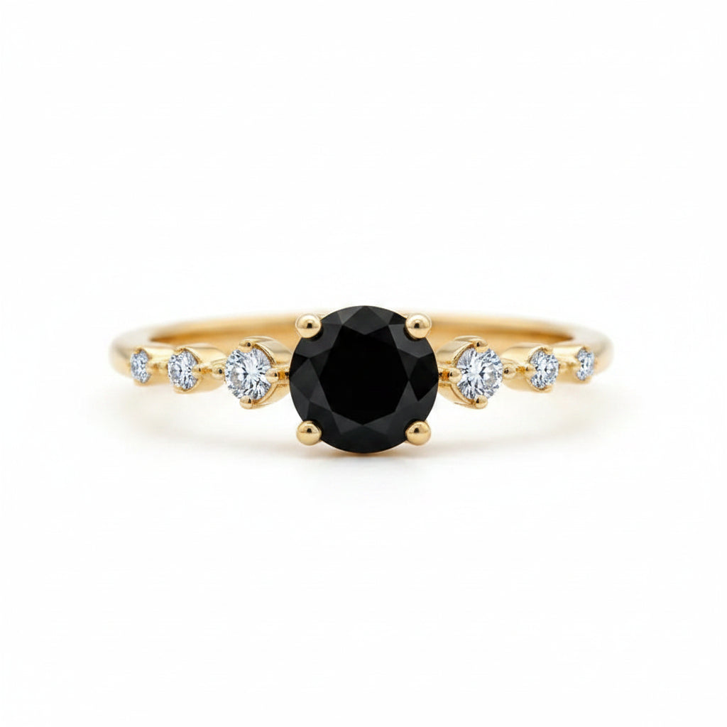 A gold ring featuring a large round black center stone and smaller clear accent stones on the band, photographed close-up on a wooden surface.