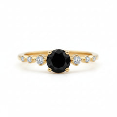 A gold ring featuring a large round black center stone and smaller clear accent stones on the band, photographed close-up on a wooden surface.