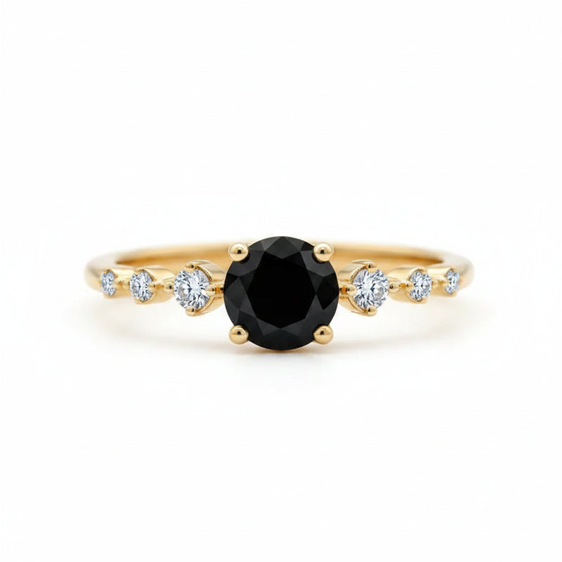 A gold ring featuring a large round black center stone and smaller clear accent stones on the band, photographed close-up on a wooden surface.